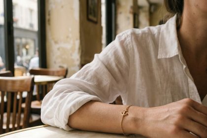 Bracelet ancre en or porté au poignet d'une femme en chemise en lin blanc dans un café parisien